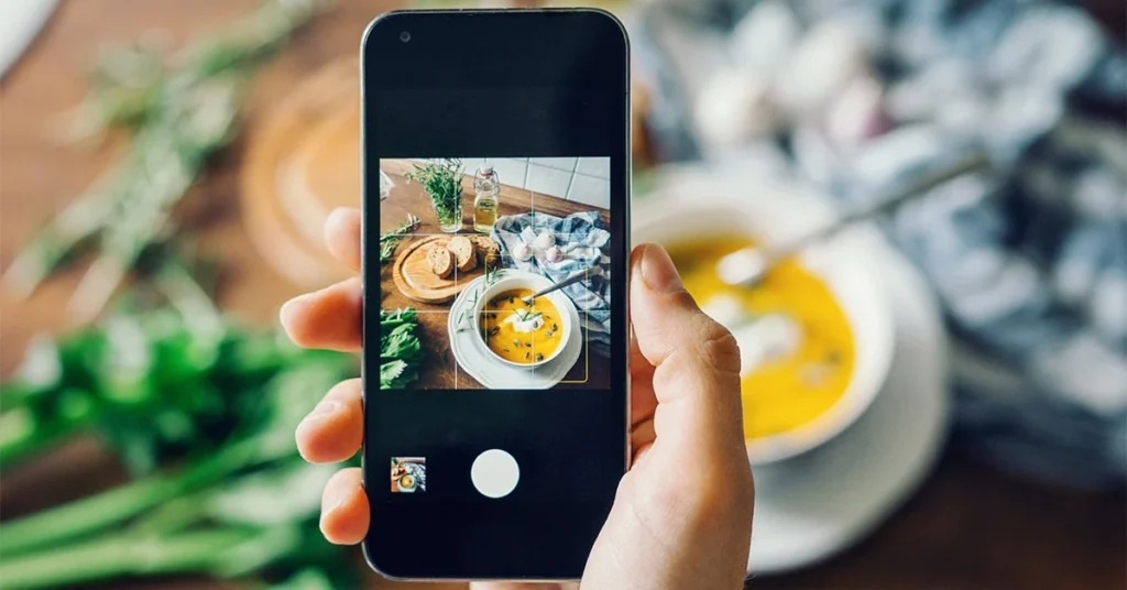 person photographing food with their smartphone and using a grid